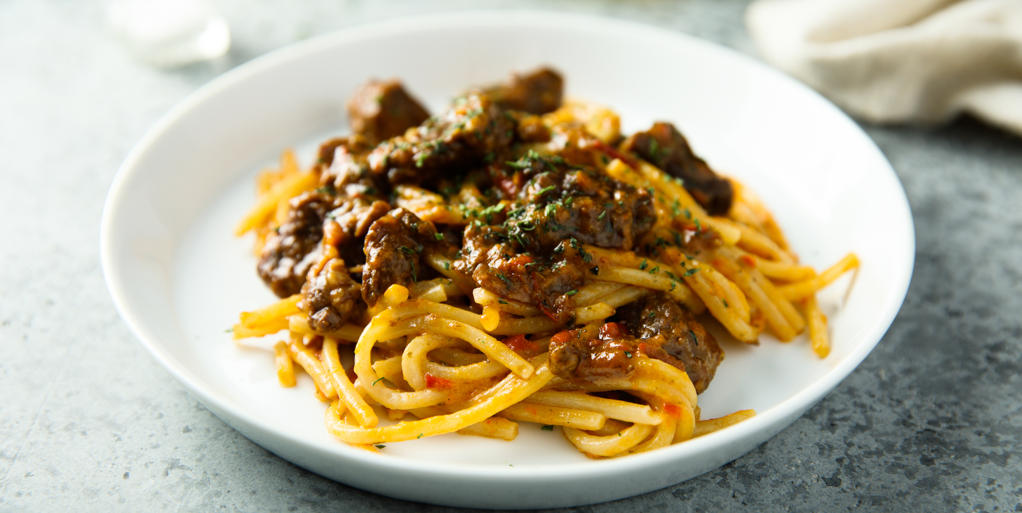 Spaghetti pasta dish with red sauce topped with meat on a clean white bowl plate 