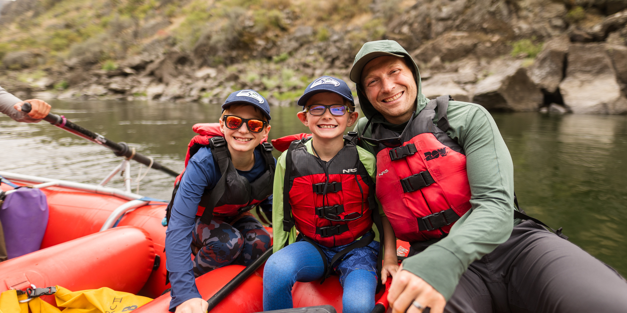 A dad and his two suns smiling for a photo atop a red raft on the Salmon River in Idaho