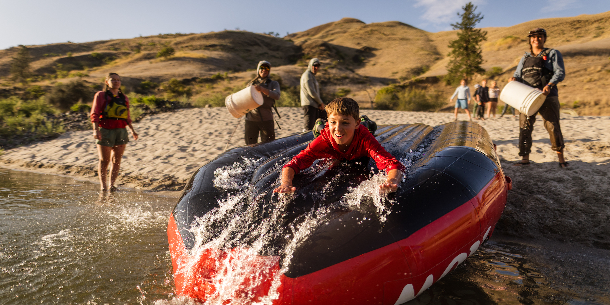 Young boy sliding down an upside down raft into the Salmon River in Idaho
