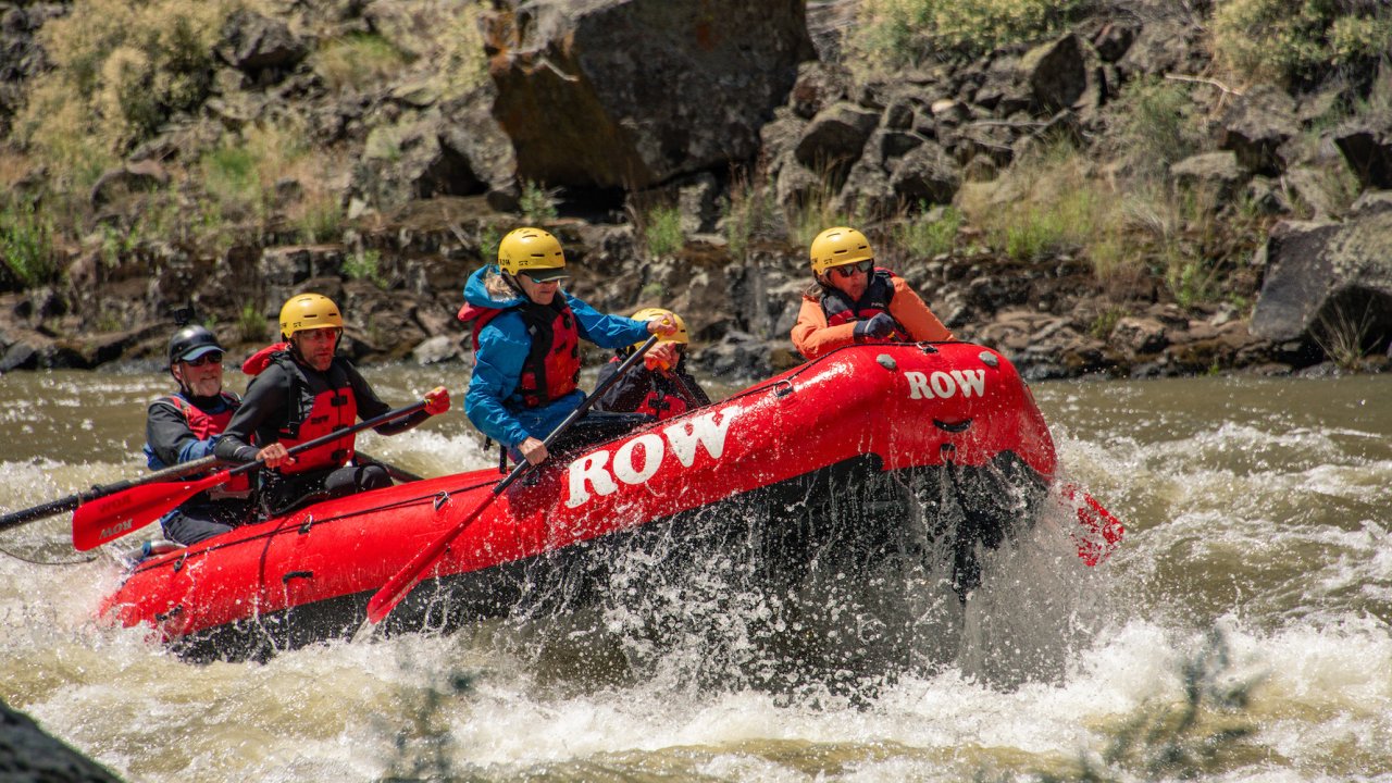 A red whitewater raft full of paddlers wearing yellow helmets paddling through a rapid in Idaho