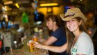 A smiling woman sitting at the bar in a brewery enjoying a beer while on a guided biking tour.