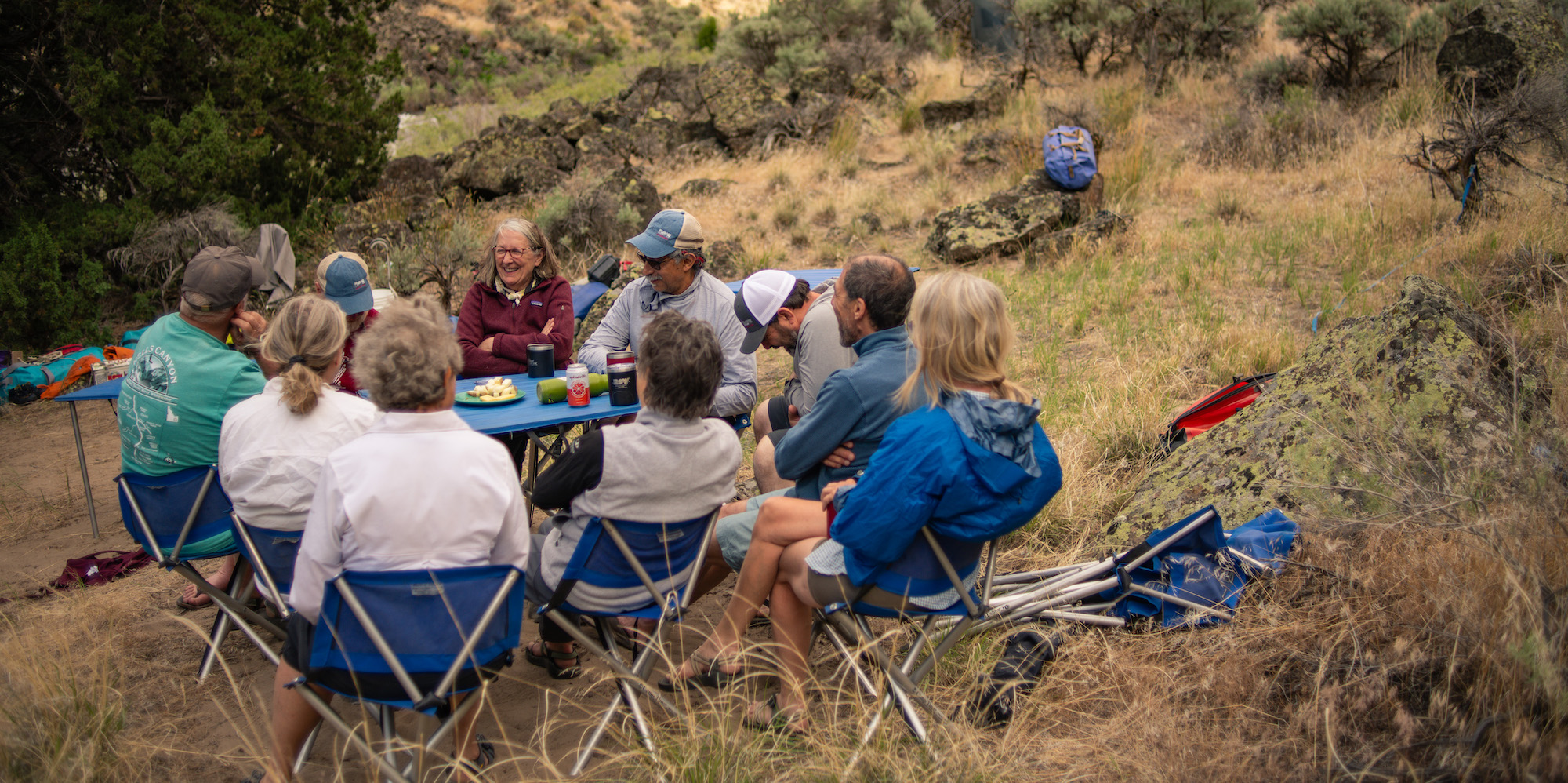 A group of rafters around a table at camp along the Bruneau River laughing with one another