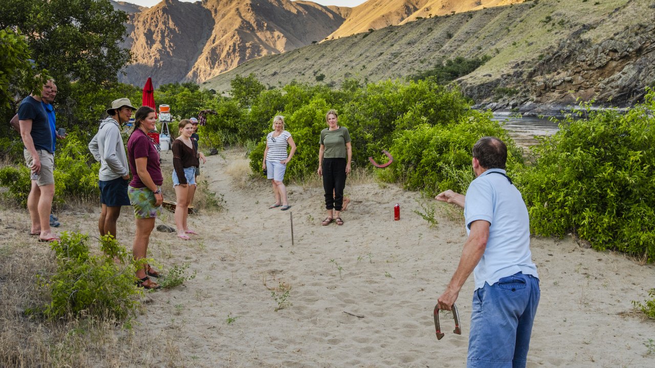 Group of guests on a multi-day rafting trip playing horseshoe at a riverside camp along the Snake River in Idaho