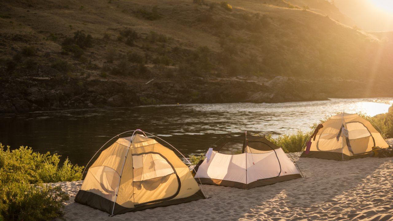 Three tents set up on a white sand beach along the Salmon River during golden hour in Idaho
