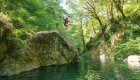Swimming hole along the Rogue River with a person jumping off of a large rock into the pool