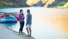 Couple standing and chatting on a sandy riverbank near colorful rafts.