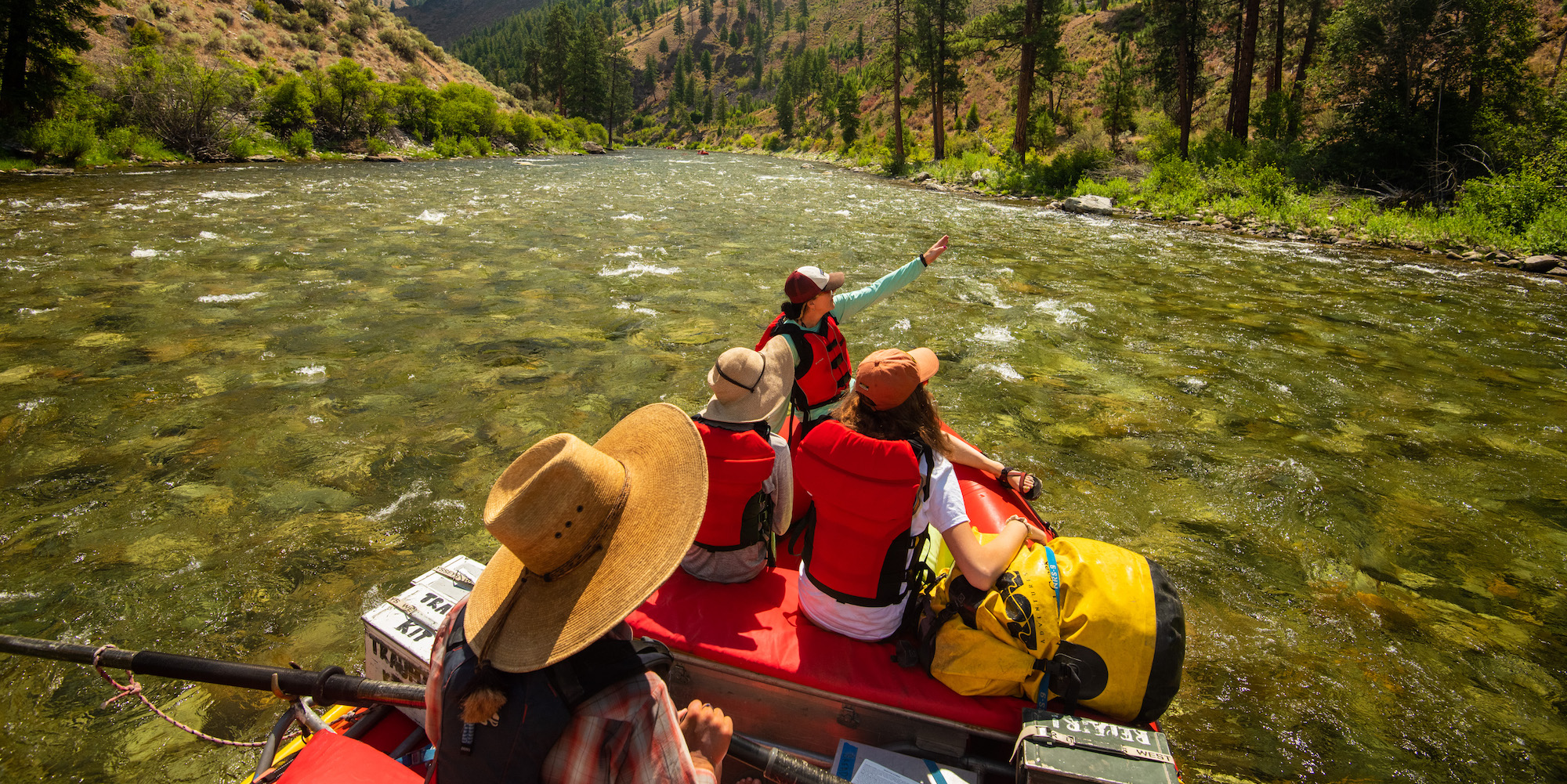 A women pointing up at something as two other girls and a guide on the oars look up river right while rafting in Idaho
