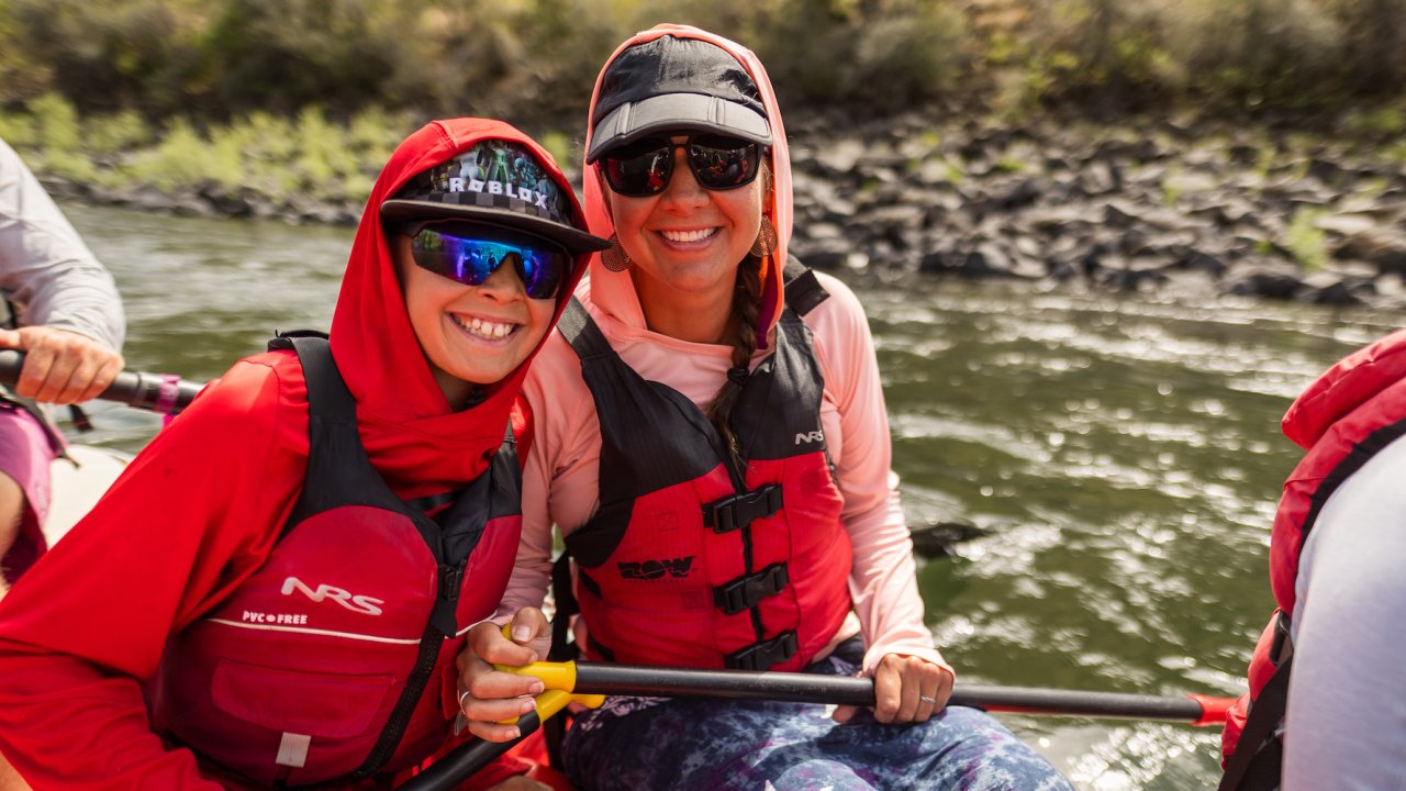 A mom and sun wearing sunglasses and smiling with each other while rafting with ROW Adventures in Idaho