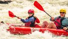 Family rafting vacation with a parent and child paddling an inflatable kayak together through whitewater rapids on a guided river trip
