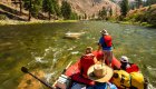Person standing up in a red raft to cast a fly fishing line while a guide rows them down the river in Idaho