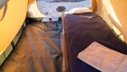 A cot set up inside of a tent with a sleeping bag, pillow, and towel set up for the tent guest