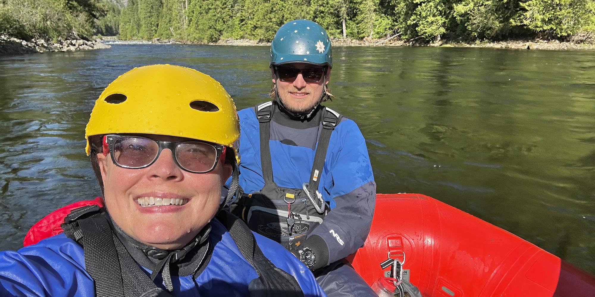 Two people dressed for a cold whitewater adventure taking a selfie on the river.