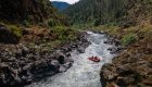 A red raft navigates whitewater rapids on the Rogue River in Oregon, surrounded by rugged canyon walls and forested hills, showcasing the thrill of Rogue River rafting adventures.