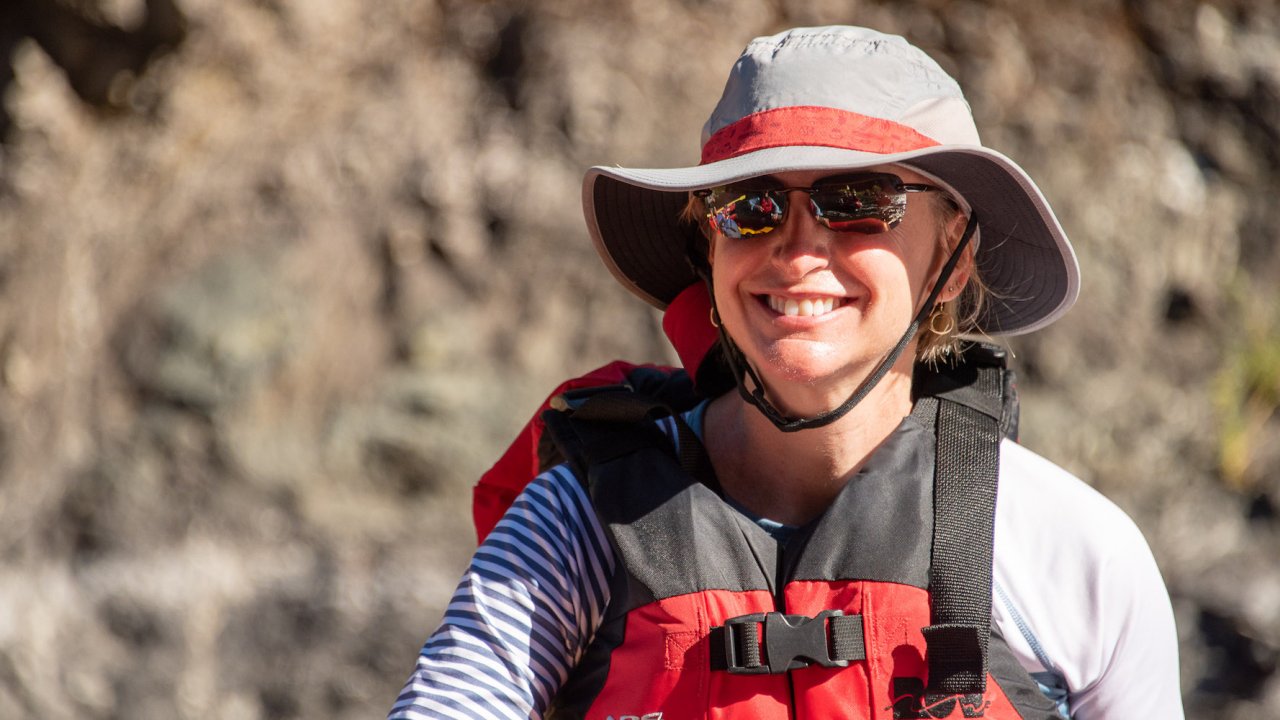 Person wearing a sun hat, PFD, and sunglasses on a river trip smiling in the sun