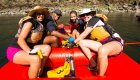 Group of rafters smiling and paddling together in a red ROW Adventures raft on Idaho’s Clearwater River, enjoying a sunny summer day on the water.