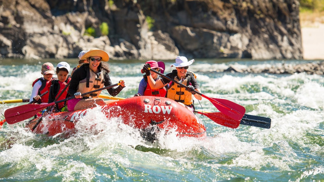 Group rafting through mild rapids with ROW Adventures on a sunny day.