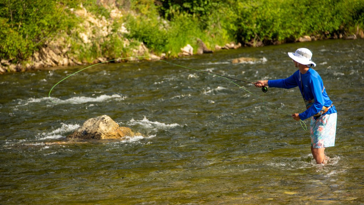 Person wading in a river while fly fishing on a sunny day
