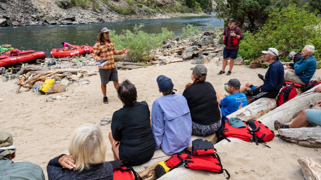 ROW Middle Fork Manager, Jake Baker, addresses the group prior to the morning departure. rafters sitting on a beach near rafts
