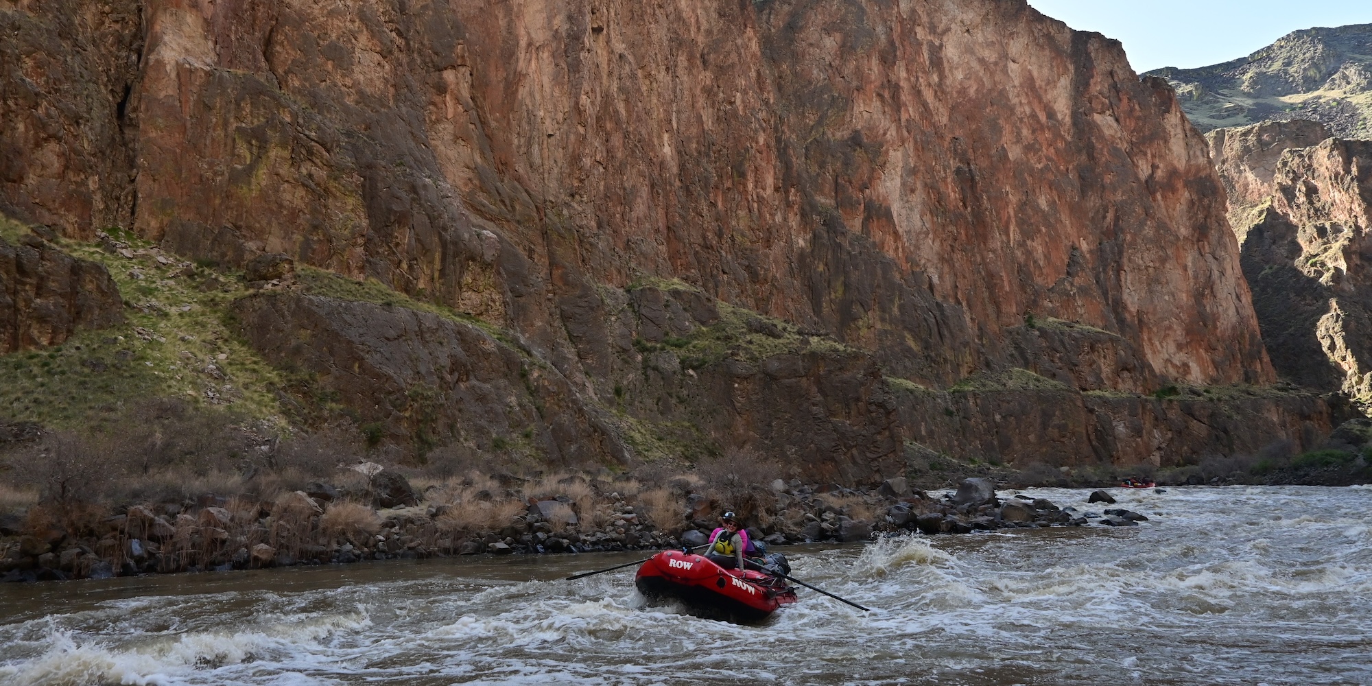 A raft navigating down the Owyhee river with steep rocky cliffs surrounding them. 