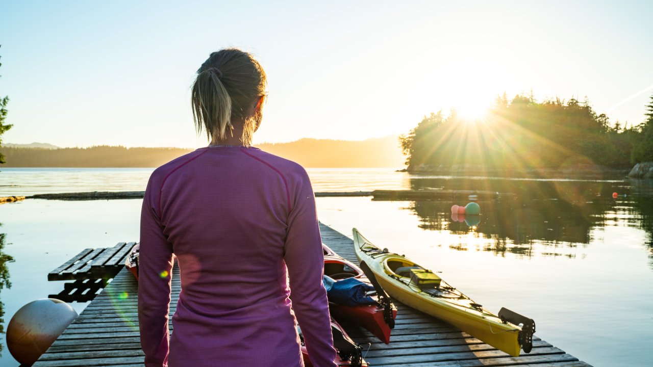 Person overlooking a dock full of sea kayaks along the Pacific Ocean at sunset