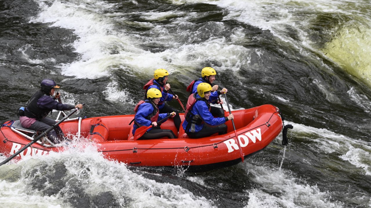 A red raft moving fast on the river with passengers