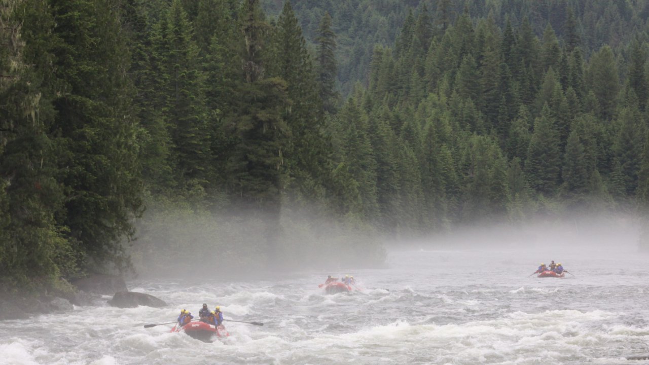 Downstream shot of two red rafts floating down the Lochsa River among dense forests on a cloudy day