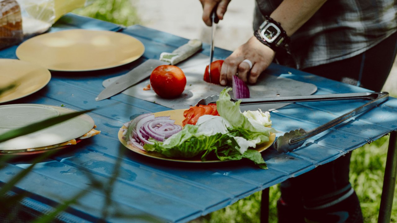 Person cutting a red onion with a lunch spread presented in front of them on a blue table