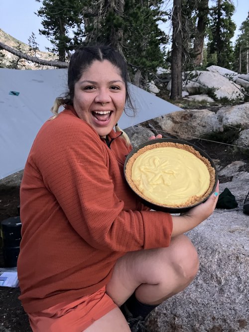 ROW Adventures employee smiling while camping and baking a cheesecake. 