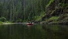 A red raft on a flat water section of river among a very dense and green forest