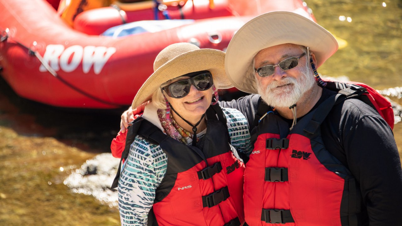 couple in pfd's standing in front of red raft