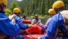 Passengers sitting on a red raft while their guide stands in the water at the bow of their boat giving a safety talk