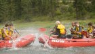 Guests on two whitewater rafts splashing each other with their paddles. 