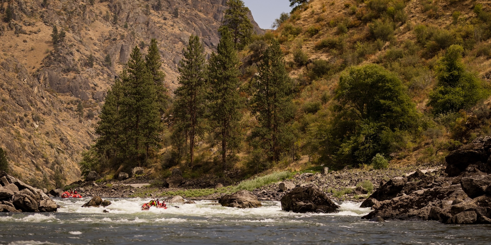 Multiple red ROW Adventure rafts navigating through a whitewater rapid in Idaho.
