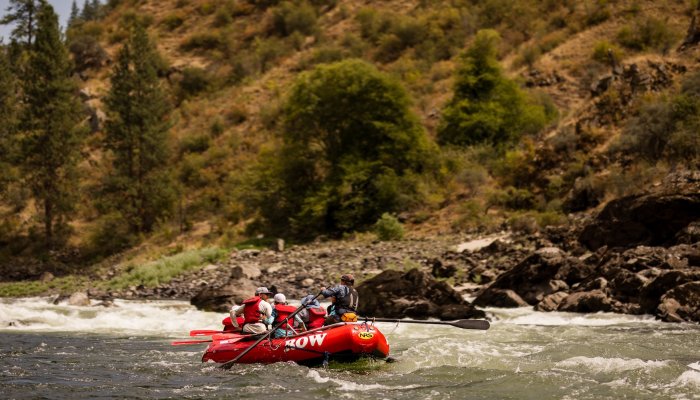 A group of people in a red whitewater raft floating downstream on an Idaho river.