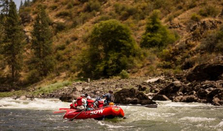 A group of people in a red whitewater raft floating downstream on an Idaho river.