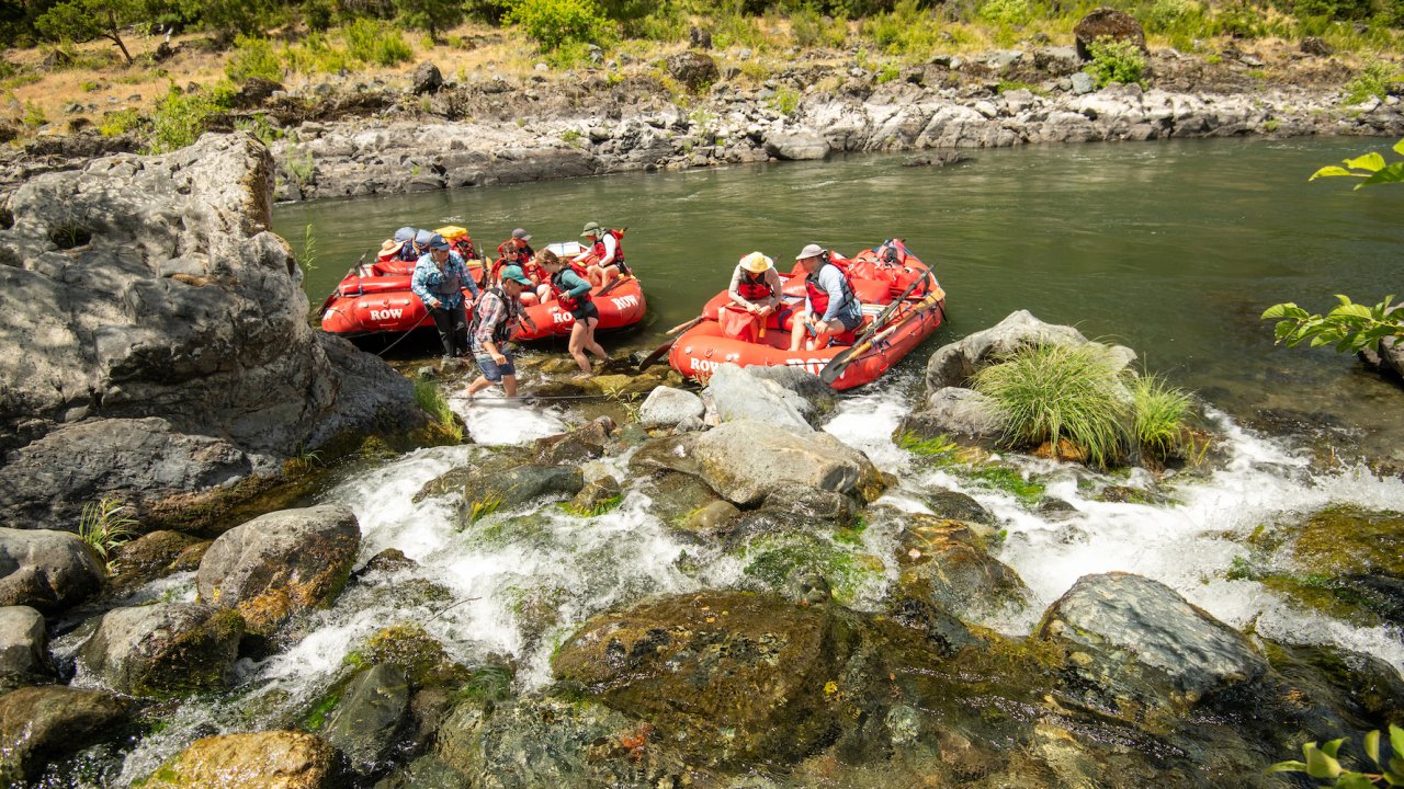 side stream flowing into the Rogue River in Oregon where people stand around red rafts