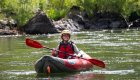 Smiling paddler in an inflatable kayak enjoying a calm stretch of the Rogue River in Oregon, a scenic spot for family-friendly Oregon rafting trips.