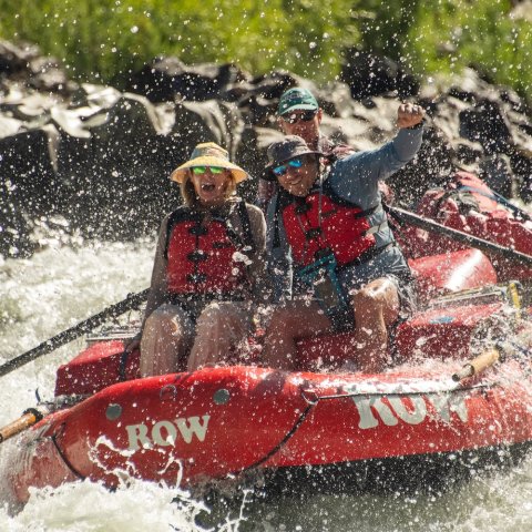 Three people in a whitewater raft going through a small rapid on the Rogue river.