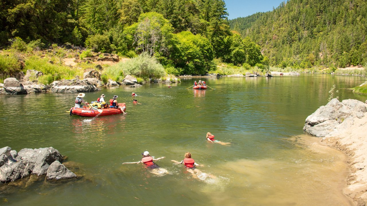 A family swimming in the Rogue River from the shore back to their red rafts in the sun