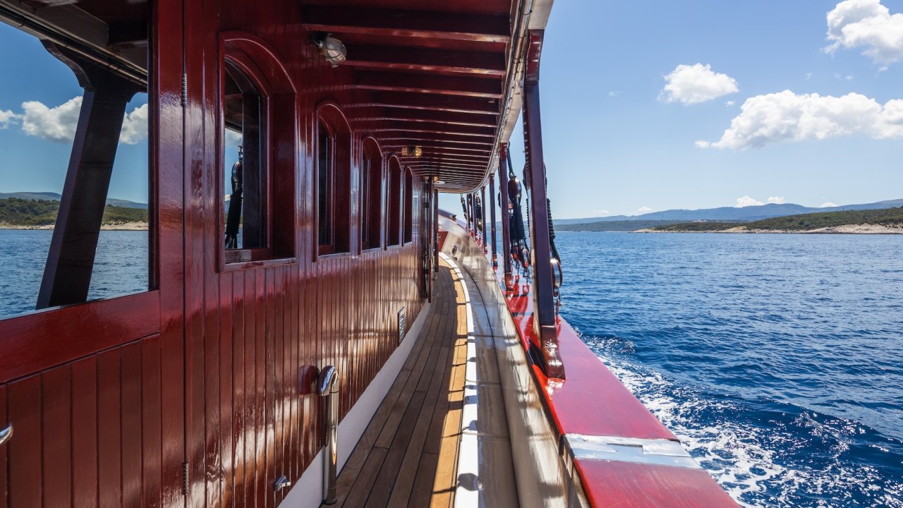 A view along the side deck of a wooden sailing yacht as it's moving through the Adriatic Sea.
