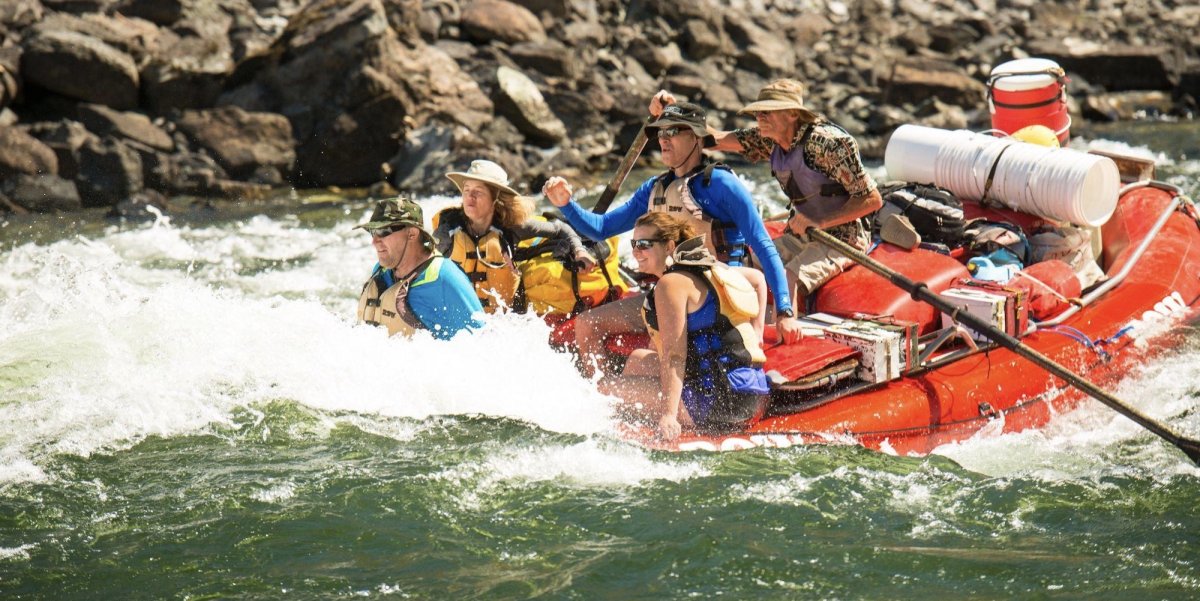 A man rowing a red raft with 4 passengers through a rapid