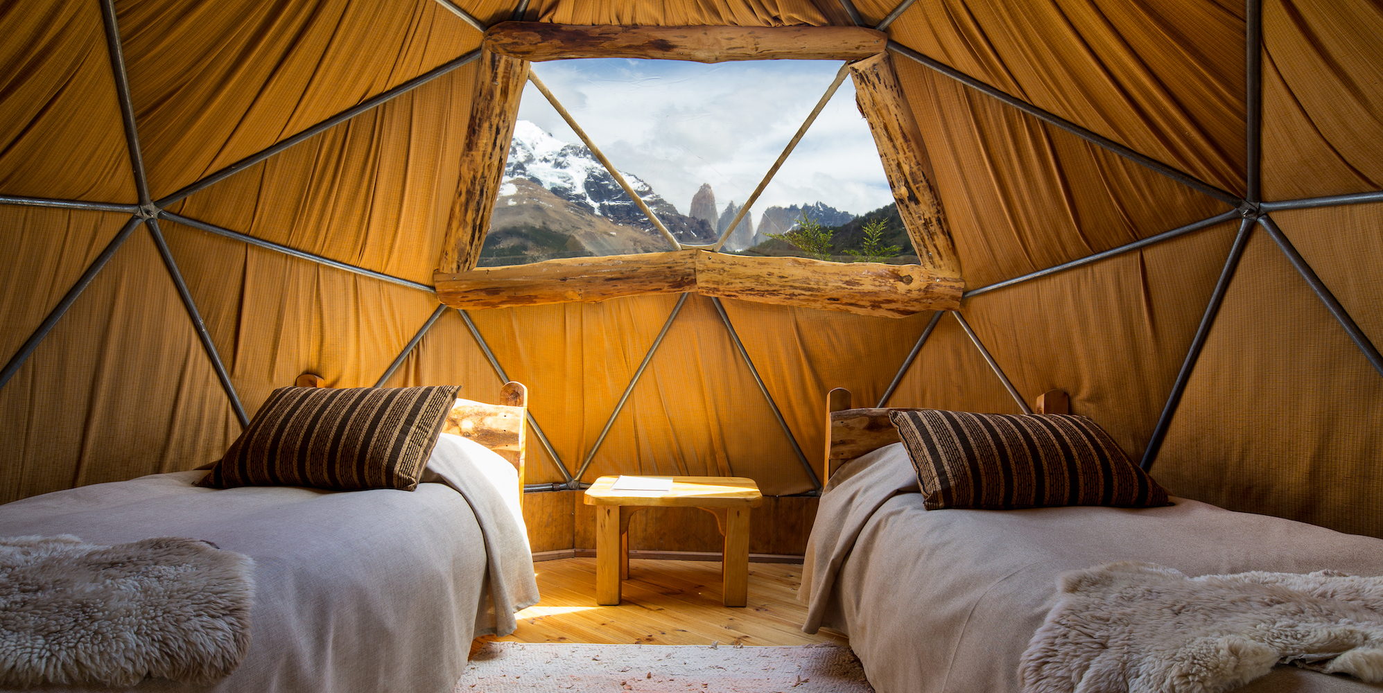 Two single beds in a luxury glamping set up with Patagonian mountains peaking through the window