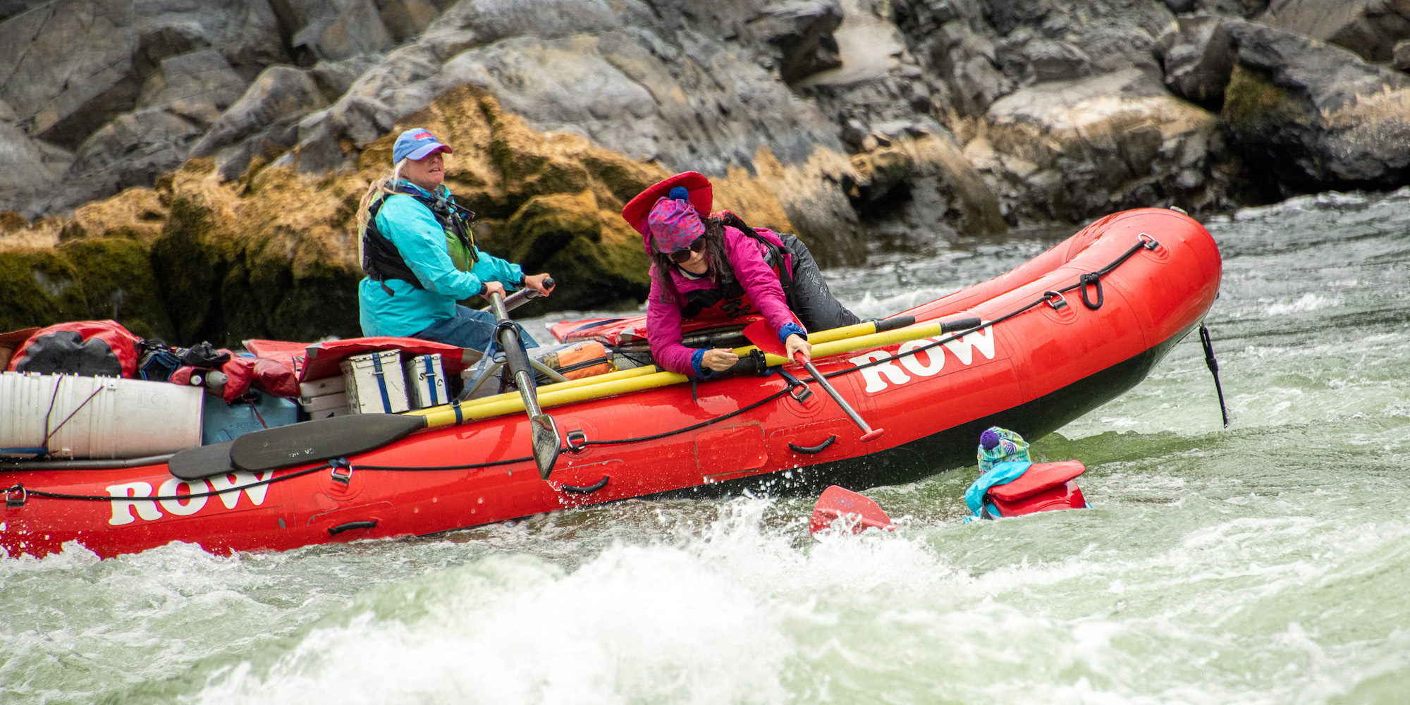 A river guide and women helping a person in a rapid get back into the boat on the Snake River