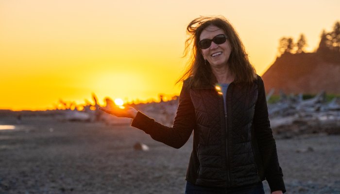 Traveler enjoying sunset at a beach on the Olympic Peninsula, Washington, with driftwood and golden skies along the Pacific coast.