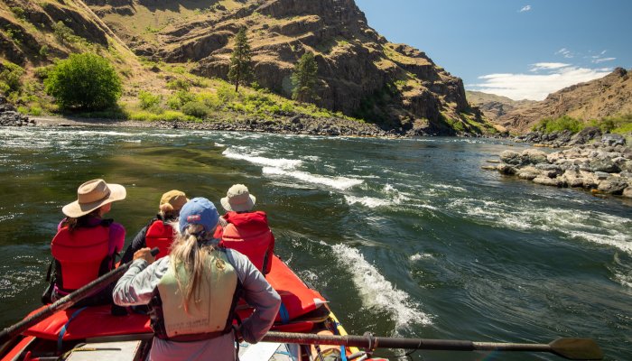 A red boat with a guide on the oars with three passengers in the front floating downstream