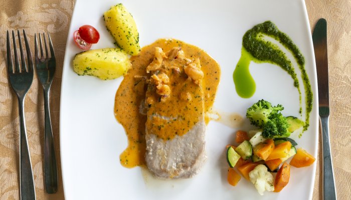 Cooked pork chop next to a side of green and orange vegetables on a white plate