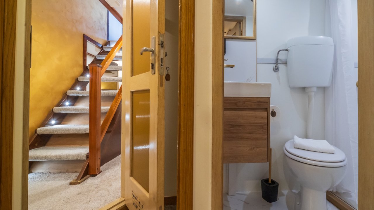 A small ensuite bathroom on a yacht with a toilet, sink, and shower, next to a staircase.